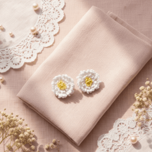 Handmade white crochet flower earrings displayed with lace, ribbons, and dried flowers for an aesthetic photoshoot.